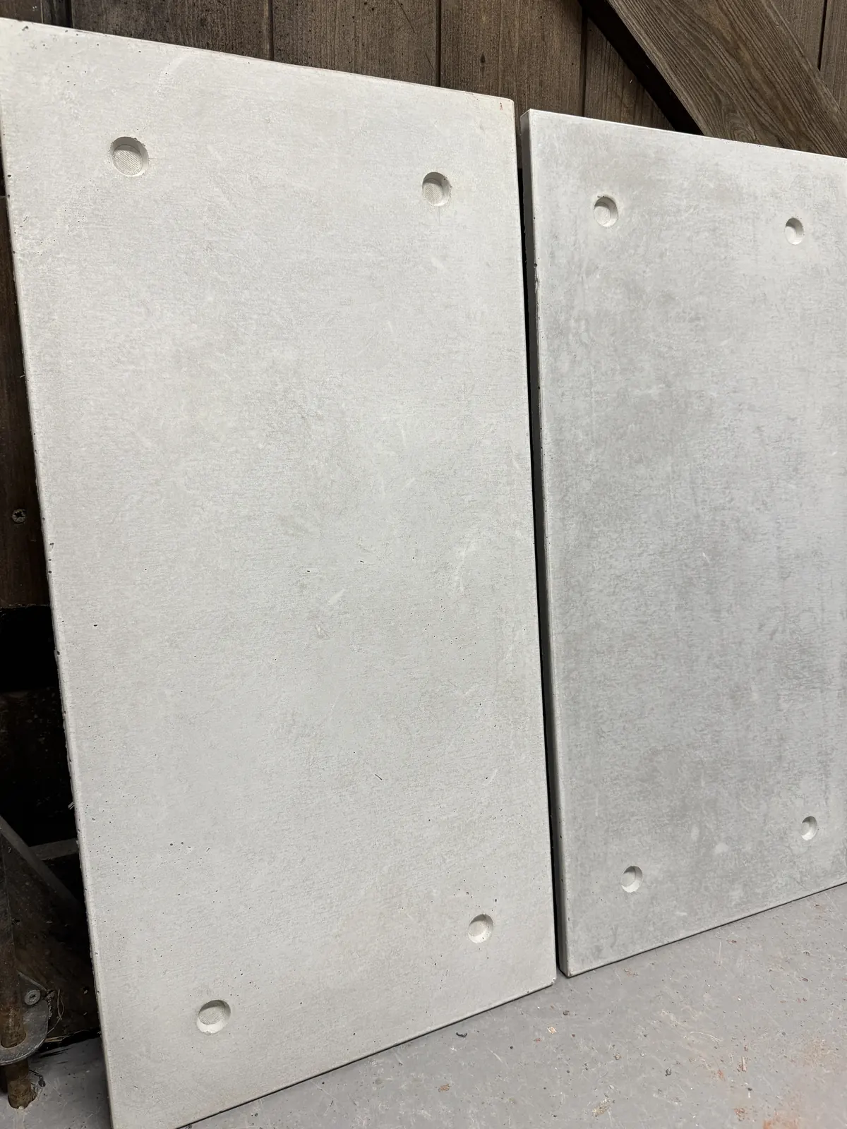 Two pale grey cast concrete cladding tiles with countersunk fixing holes, ROKA Studio workshop