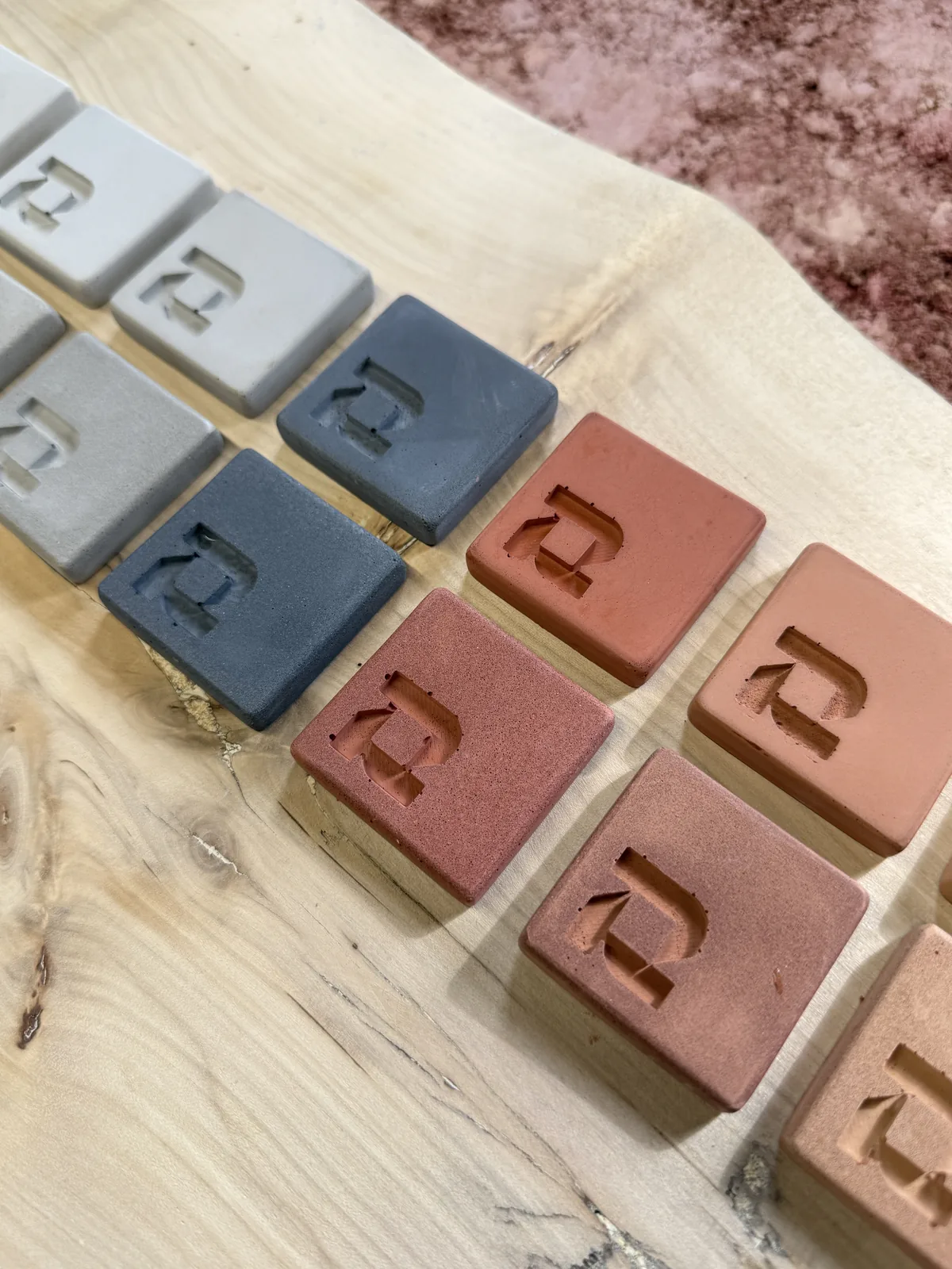 Angled close-up of ROKA concrete samples in grey, charcoal and terracotta, showing both finishes